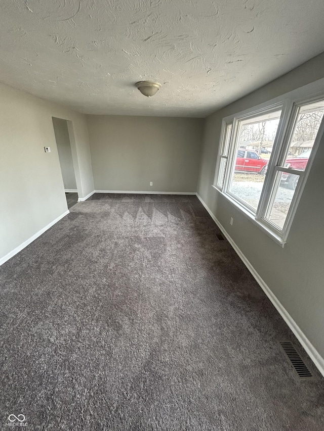 spare room featuring a textured ceiling, dark colored carpet, visible vents, and baseboards