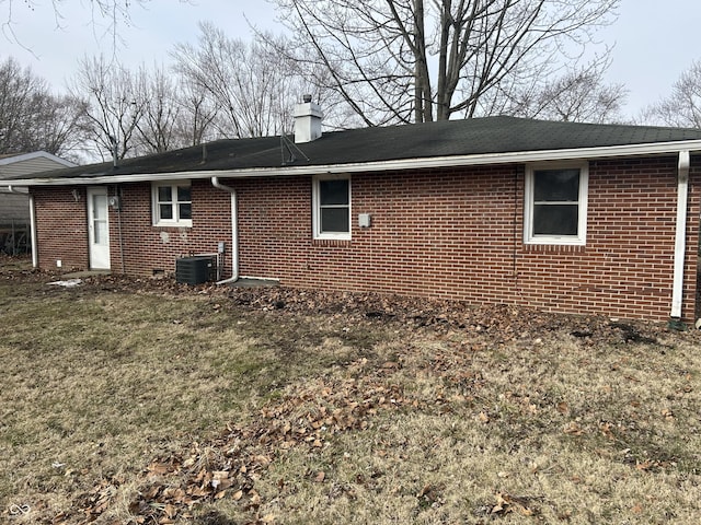 view of side of home featuring cooling unit, brick siding, a lawn, and a chimney