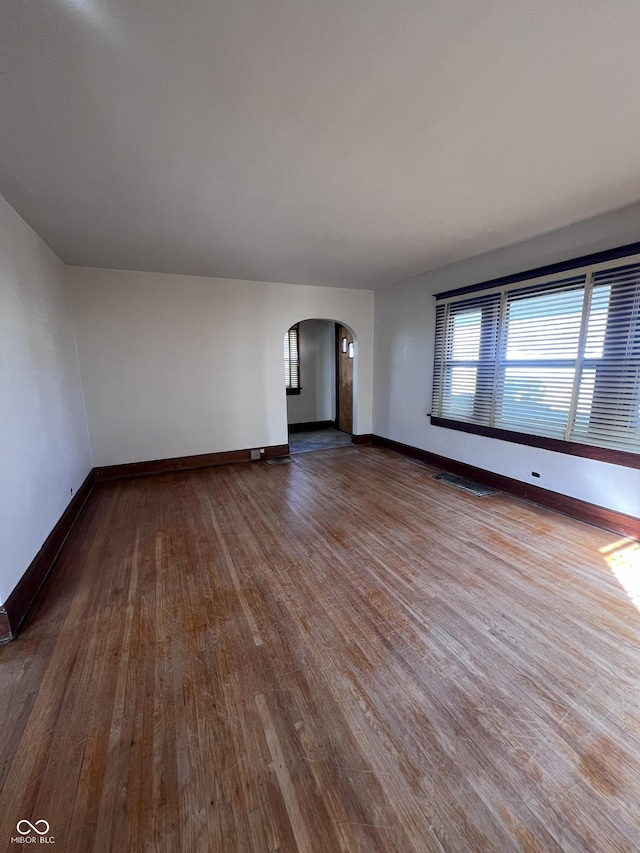 unfurnished living room featuring arched walkways, dark wood-style flooring, visible vents, and baseboards