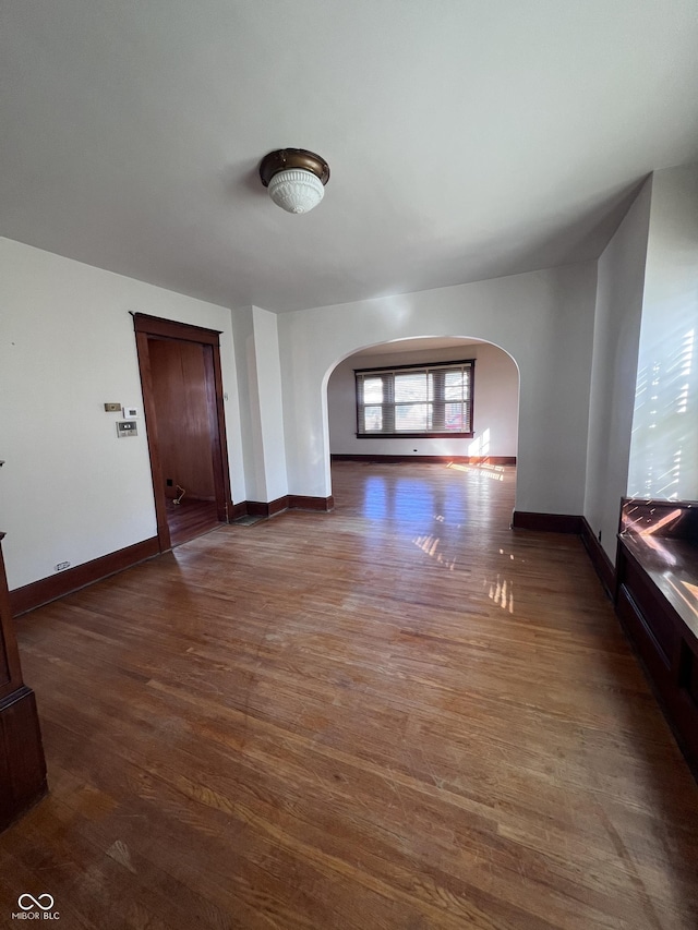 unfurnished living room with arched walkways, baseboards, and wood finished floors