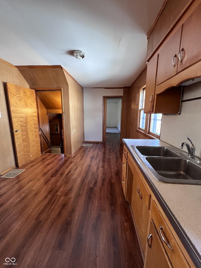 kitchen with dark wood-style flooring, brown cabinets, light countertops, a sink, and wooden walls