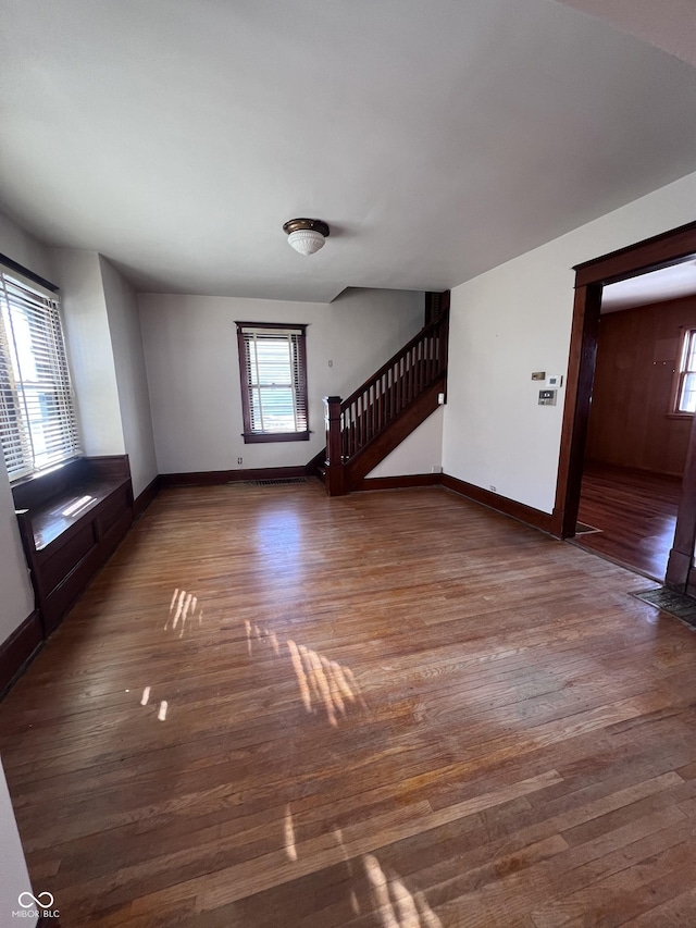 unfurnished living room featuring stairs, baseboards, and wood finished floors