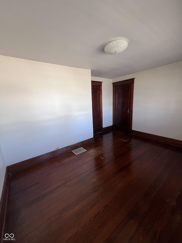 spare room featuring dark wood-type flooring, visible vents, and baseboards