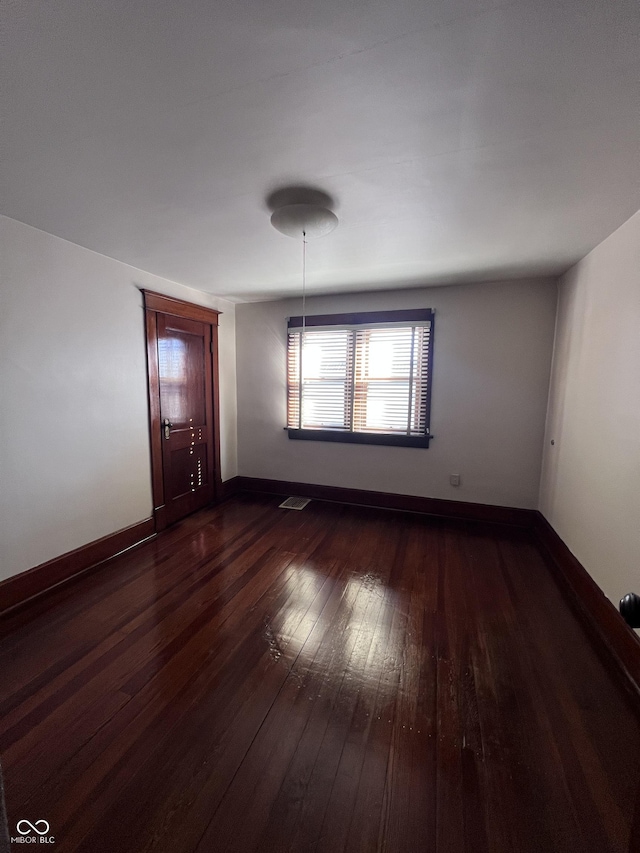 empty room featuring dark wood-style floors, visible vents, and baseboards