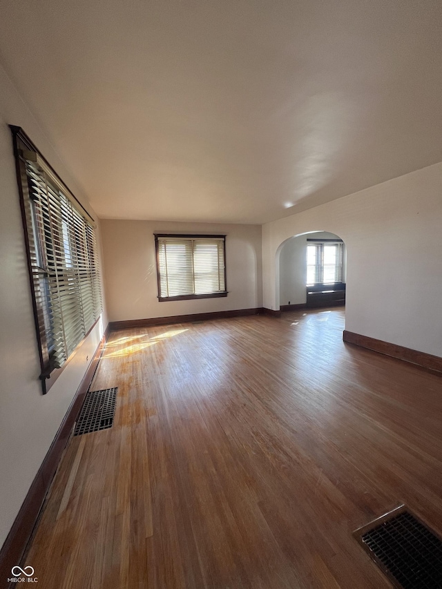 unfurnished room with arched walkways, visible vents, baseboards, and wood finished floors