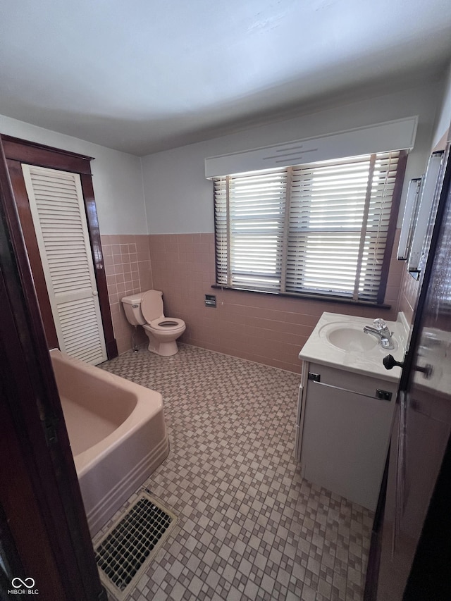 bathroom featuring toilet, a wainscoted wall, vanity, tile walls, and a tub