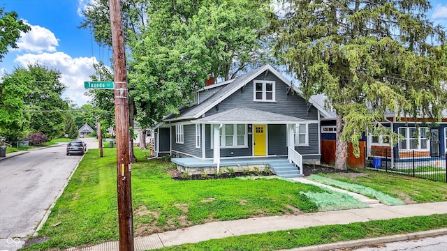 bungalow-style house with a front yard, fence, roof with shingles, covered porch, and a chimney