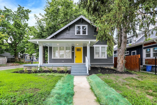 bungalow-style home with covered porch, a front yard, and fence