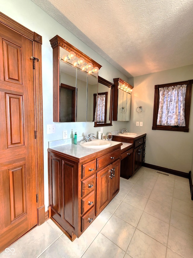 bathroom featuring visible vents, baseboards, vanity, tile patterned floors, and a textured ceiling