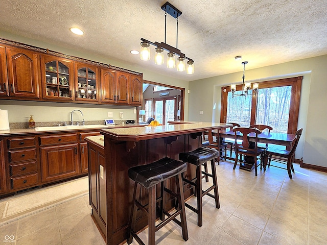 kitchen featuring a center island, glass insert cabinets, a breakfast bar, hanging light fixtures, and a sink