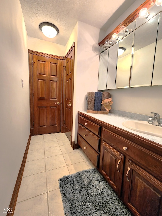 bathroom with tile patterned flooring, vanity, baseboards, and a textured ceiling