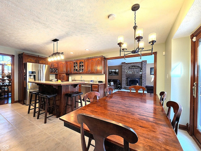 dining room featuring a brick fireplace, baseboards, a chandelier, wet bar, and a textured ceiling