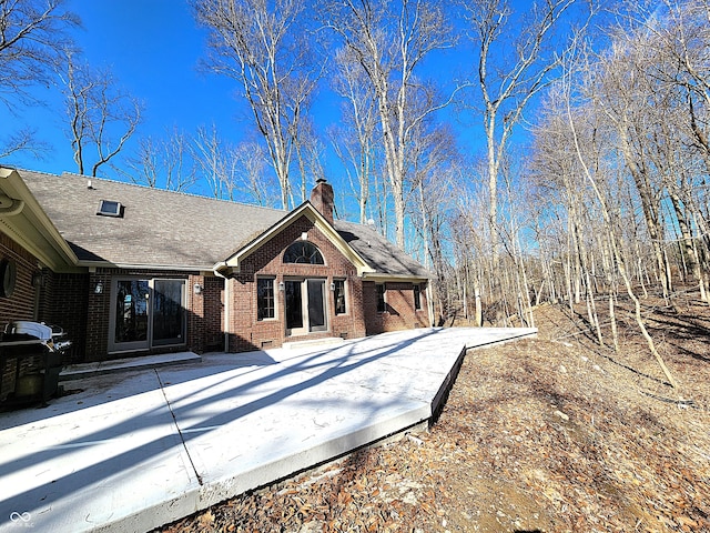 back of house with brick siding, crawl space, a chimney, and a shingled roof