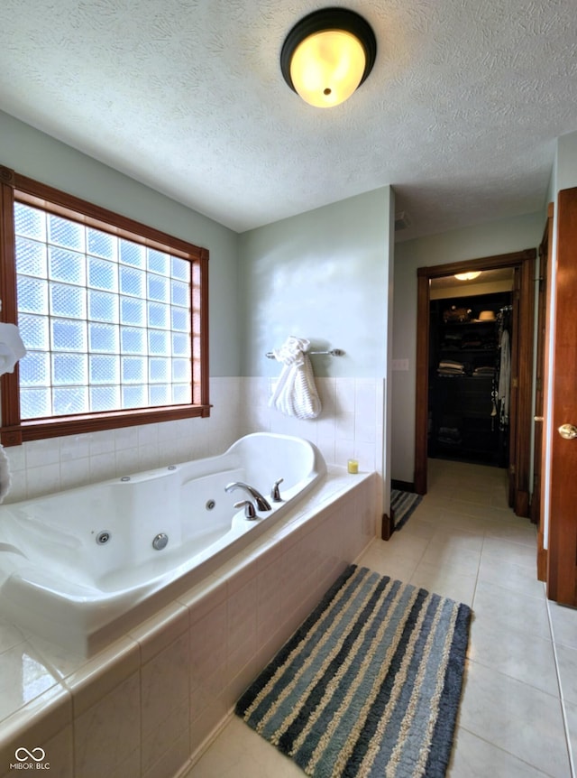 bathroom featuring a walk in closet, tile patterned floors, a jetted tub, and a textured ceiling