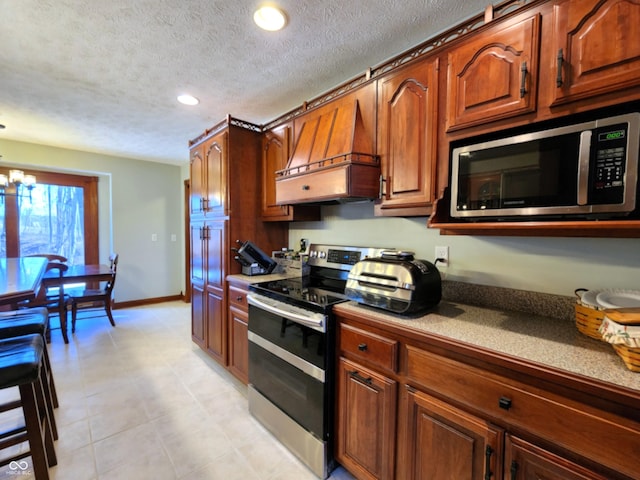 kitchen with baseboards, premium range hood, stainless steel appliances, a textured ceiling, and a chandelier