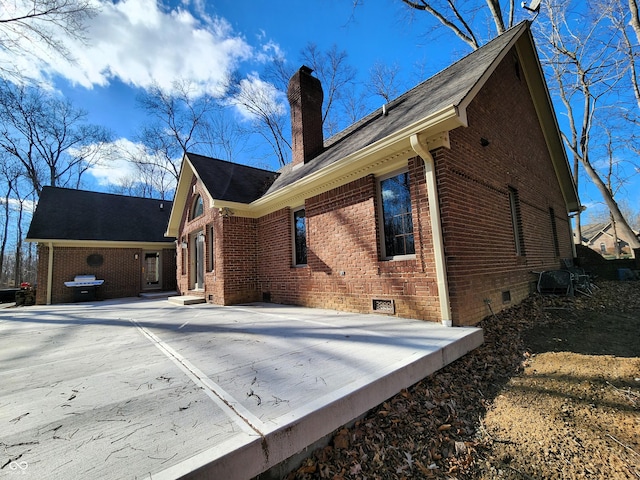 view of home's exterior featuring concrete driveway, brick siding, a chimney, and crawl space