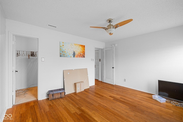 unfurnished bedroom with wood finished floors, visible vents, ceiling fan, a spacious closet, and a textured ceiling