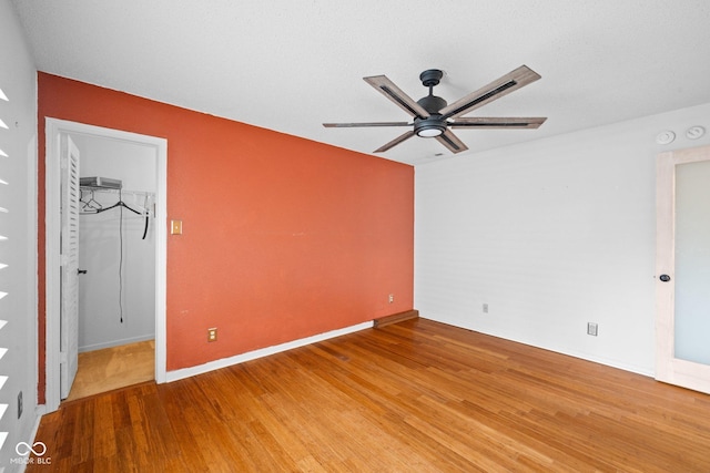 unfurnished bedroom with light wood-type flooring, a walk in closet, a closet, baseboards, and ceiling fan