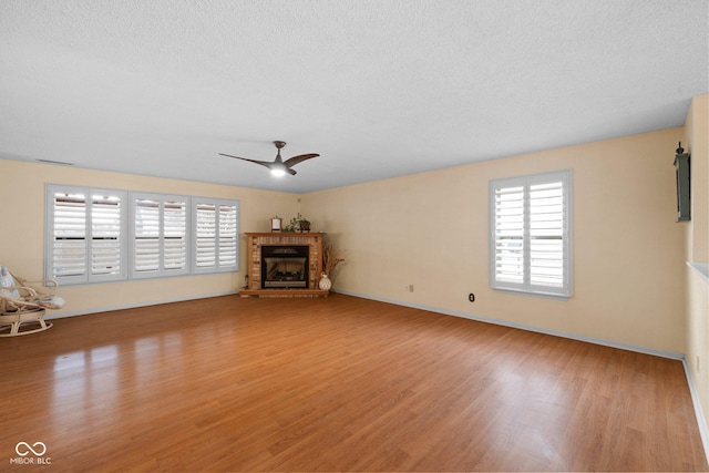 unfurnished living room with ceiling fan, light wood-style floors, a fireplace with raised hearth, and a textured ceiling