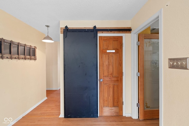 hallway featuring a barn door, baseboards, a textured ceiling, and wood finished floors