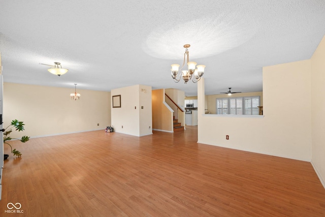 unfurnished living room featuring stairs, ceiling fan with notable chandelier, wood finished floors, and a textured ceiling