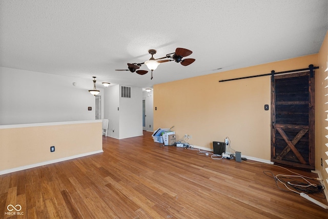 unfurnished living room with visible vents, ceiling fan, a barn door, wood finished floors, and a textured ceiling