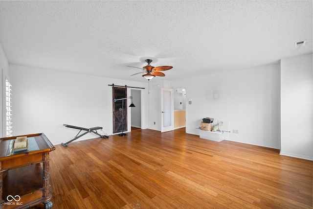 unfurnished living room featuring wood finished floors, visible vents, ceiling fan, a textured ceiling, and a barn door