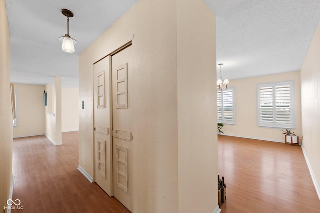 hallway with an inviting chandelier, wood finished floors, and baseboards