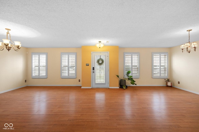 entrance foyer with baseboards, a textured ceiling, an inviting chandelier, and wood finished floors