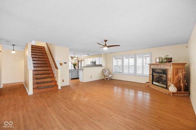 unfurnished living room with a glass covered fireplace, stairs, light wood-type flooring, and ceiling fan