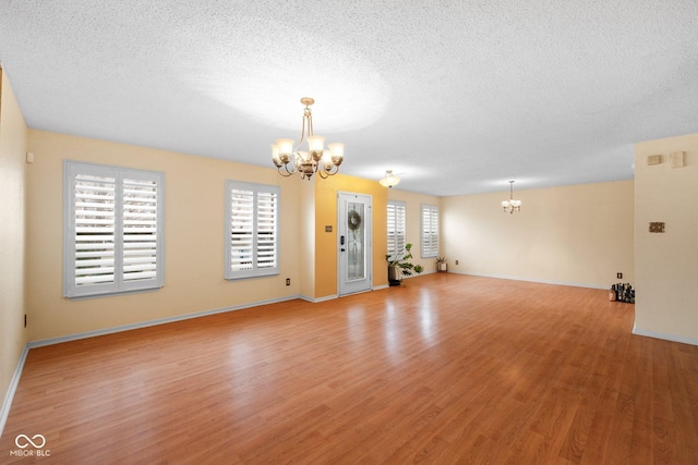 unfurnished living room with baseboards, a textured ceiling, light wood-style floors, and an inviting chandelier