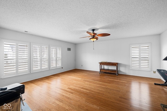 living room featuring a textured ceiling, wood finished floors, visible vents, and ceiling fan