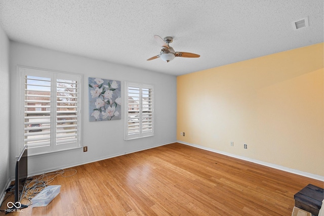 unfurnished room featuring baseboards, visible vents, ceiling fan, a textured ceiling, and light wood-type flooring