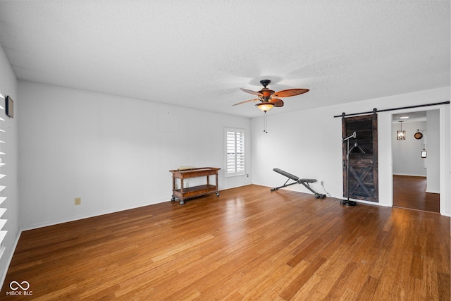 unfurnished room with a ceiling fan, a barn door, light wood-style floors, and a textured ceiling