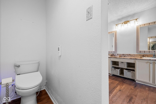 bathroom with vanity, wood finished floors, a textured ceiling, toilet, and a textured wall