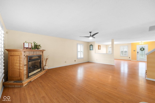 unfurnished living room with light wood finished floors, a glass covered fireplace, baseboards, and ceiling fan