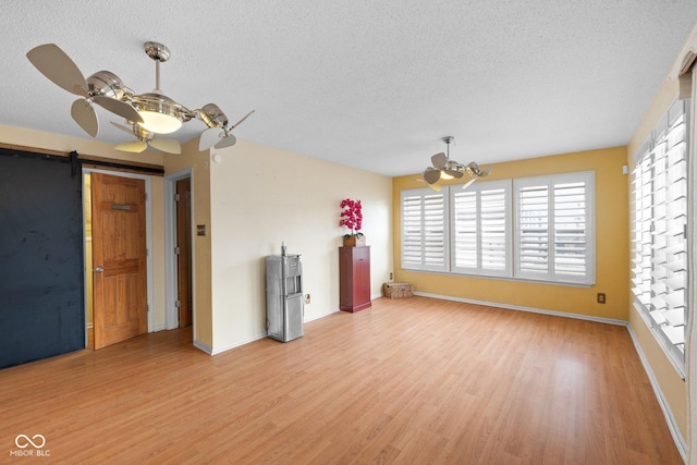 interior space with baseboards, ceiling fan, a textured ceiling, a barn door, and light wood-type flooring