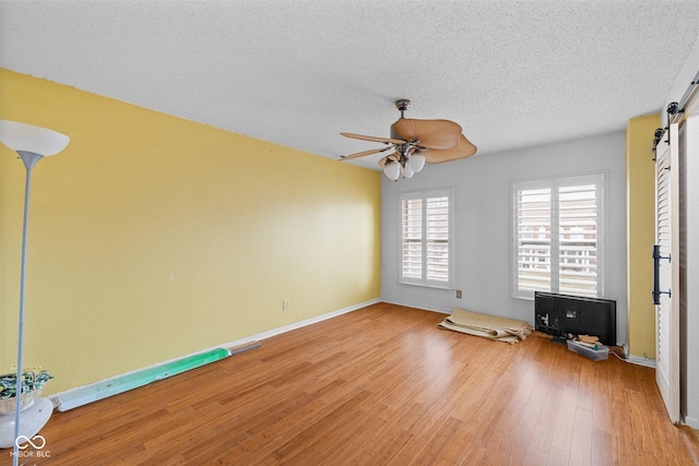 interior space featuring a ceiling fan, baseboards, a textured ceiling, a barn door, and light wood-type flooring