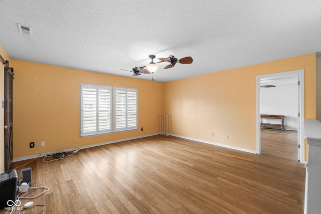 spare room featuring visible vents, light wood-style flooring, a ceiling fan, a textured ceiling, and a barn door