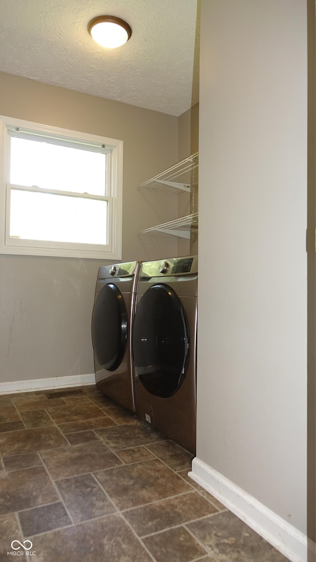 clothes washing area with laundry area, baseboards, stone finish floor, a textured ceiling, and separate washer and dryer