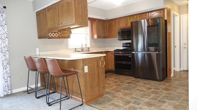 kitchen featuring brown cabinetry, appliances with stainless steel finishes, a peninsula, light countertops, and a sink