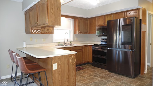 kitchen with brown cabinets, light countertops, appliances with stainless steel finishes, a sink, and a peninsula