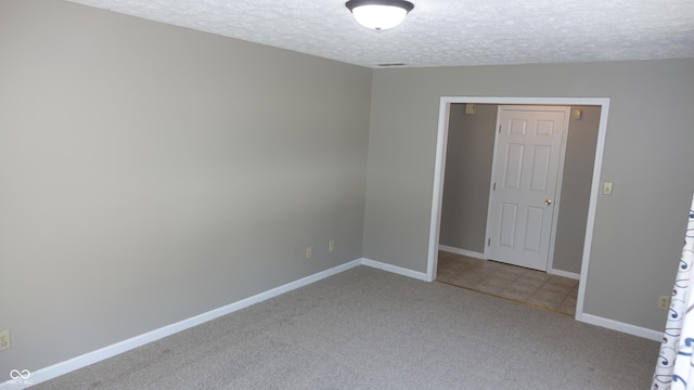 spare room with carpet flooring, a textured ceiling, baseboards, and tile patterned floors