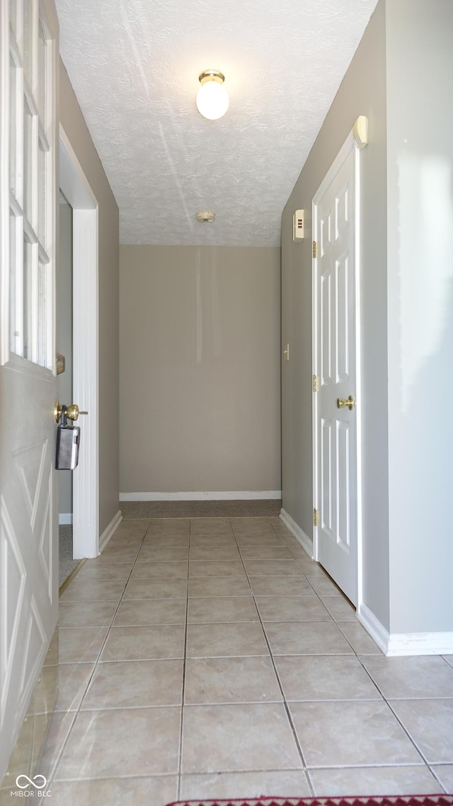 corridor featuring a textured ceiling, light tile patterned flooring, and baseboards