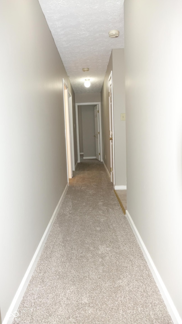 hall featuring a textured ceiling, carpet floors, and baseboards