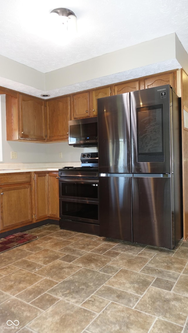 kitchen with stainless steel appliances, light countertops, stone finish flooring, and brown cabinets