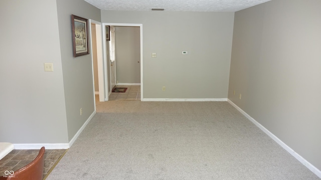 unfurnished room featuring a textured ceiling, carpet floors, visible vents, and baseboards