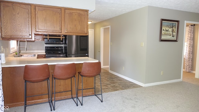 kitchen featuring light countertops, freestanding refrigerator, a sink, a textured ceiling, and range with electric cooktop