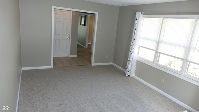 unfurnished room with a textured ceiling, carpet flooring, and baseboards