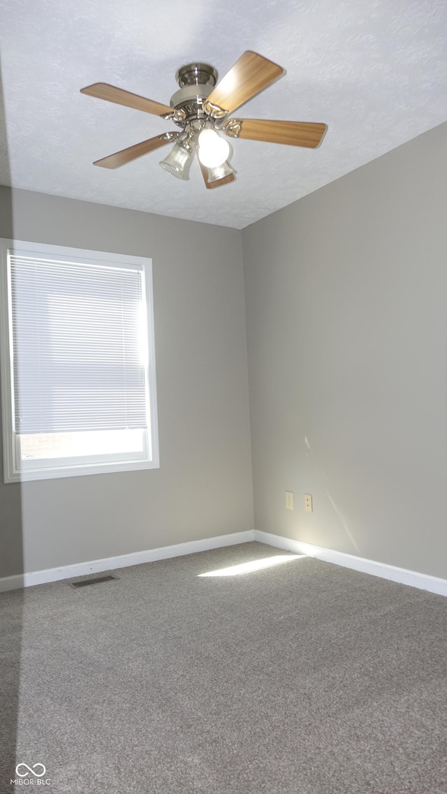 carpeted spare room featuring visible vents, baseboards, ceiling fan, and a textured ceiling